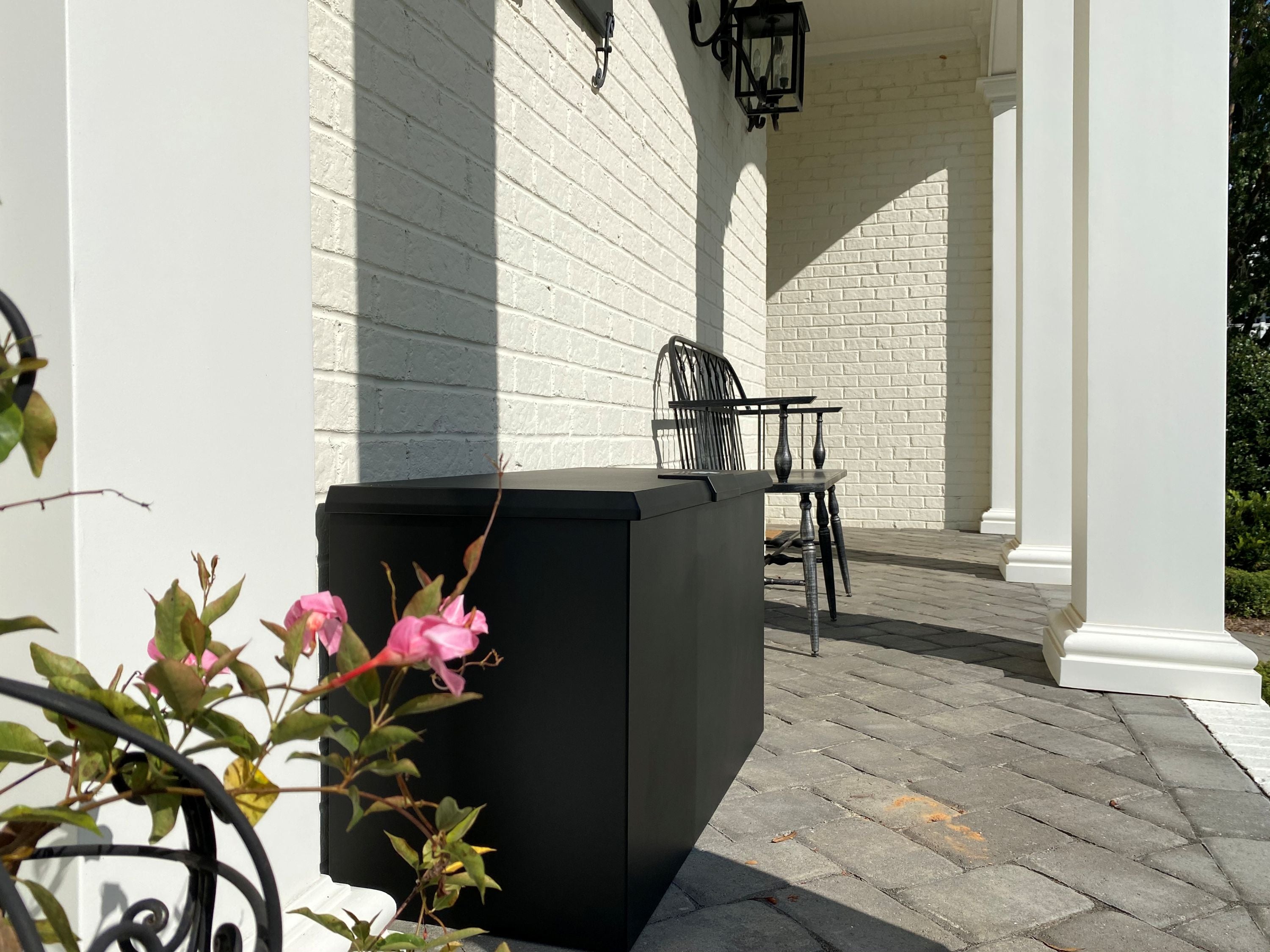 Black Loxx Boxx X-Large on a patio with a white wall and pink flowers in the foreground.