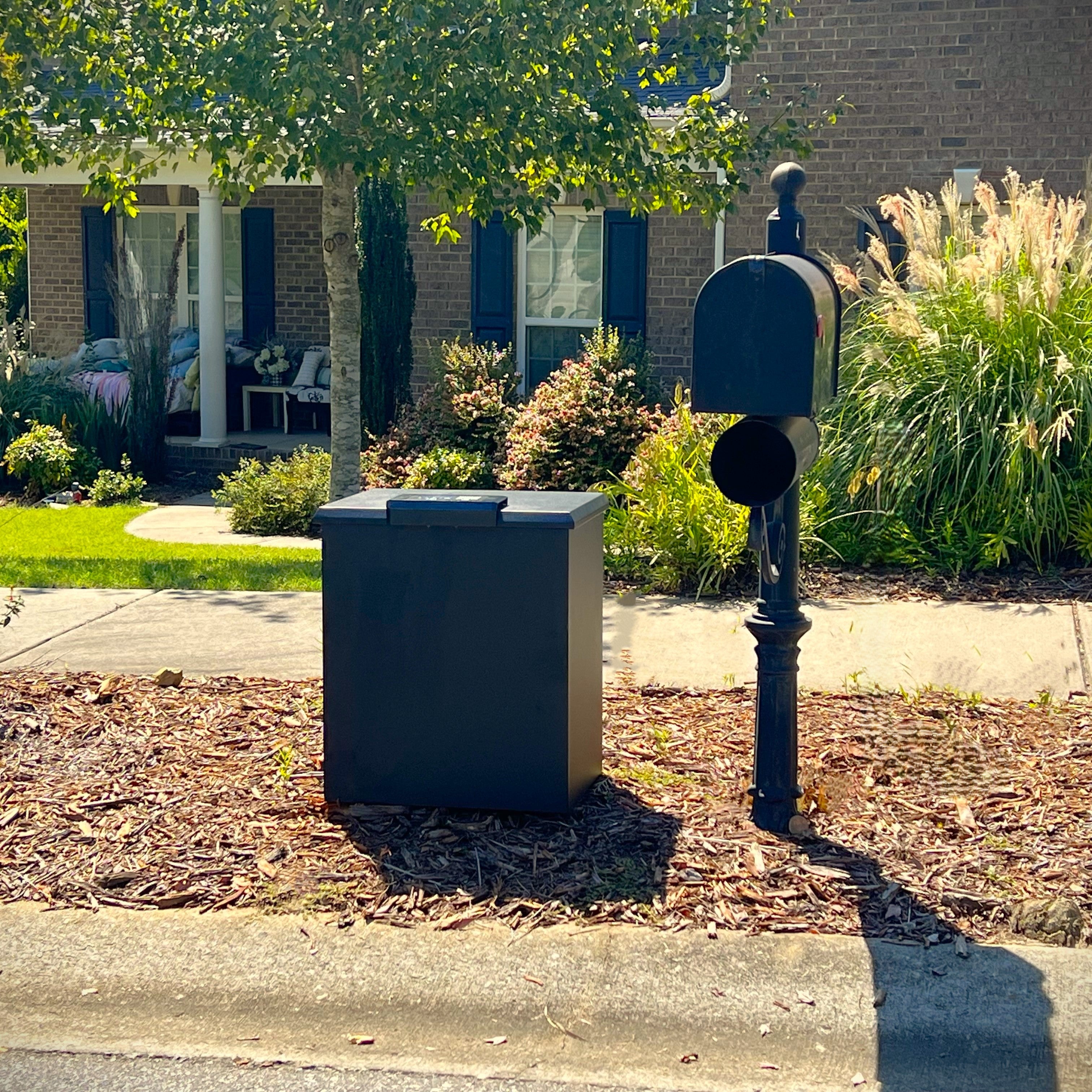 Black Loxx Boxx curbside with mailbox in front of a house with greenery.