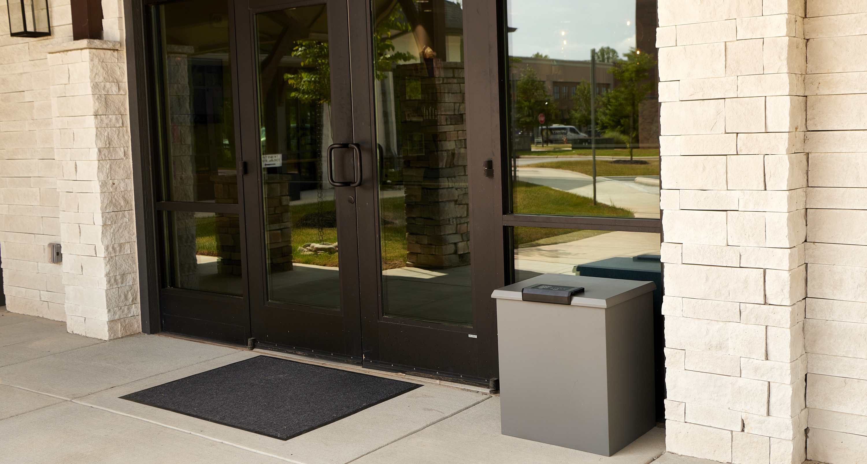 Commercial entrance with glass doors and a Loxx Boxx on a stone-paved area.