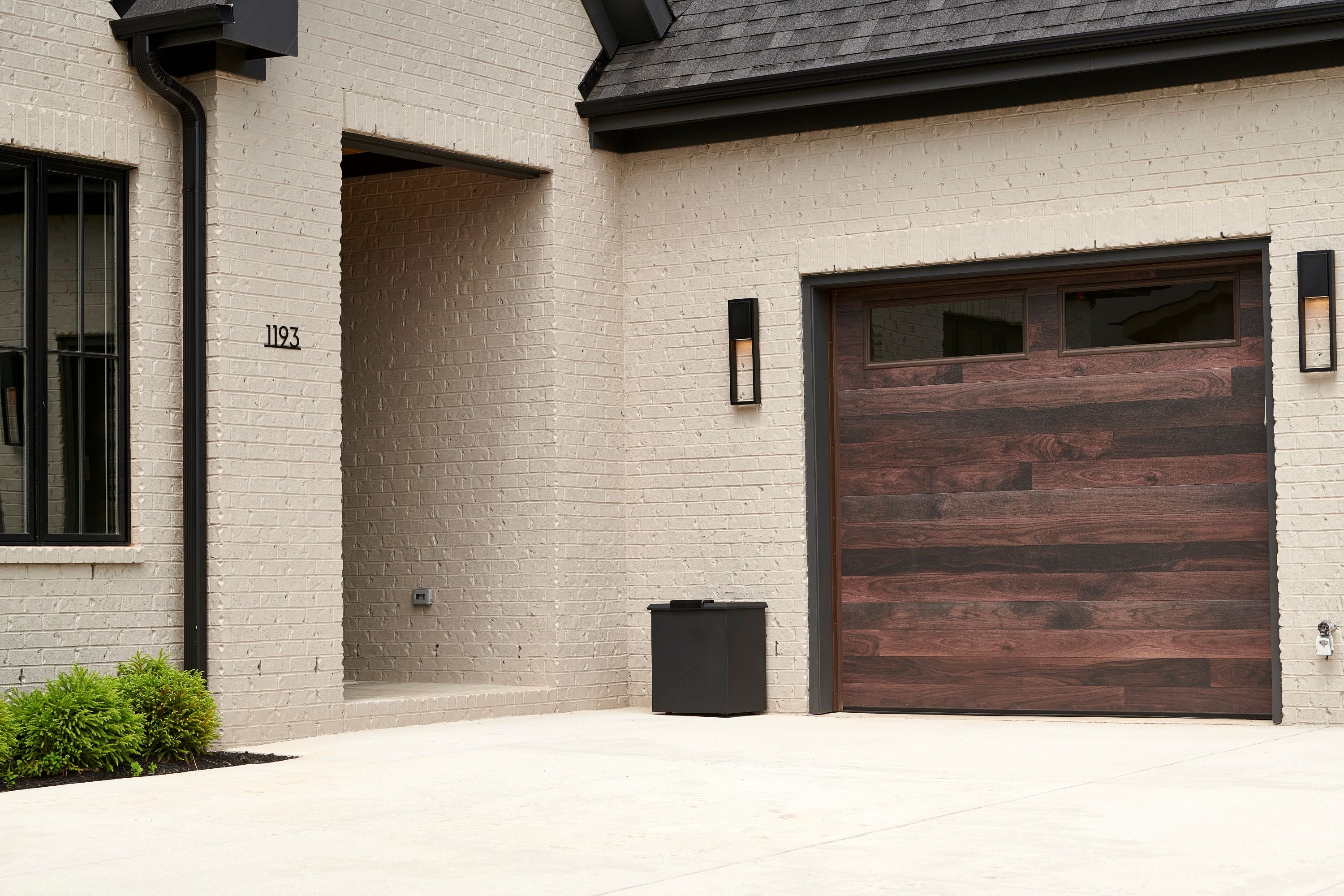 Loxx Boxx by a Modern house exterior with a wooden garage door and light-colored brick wall.