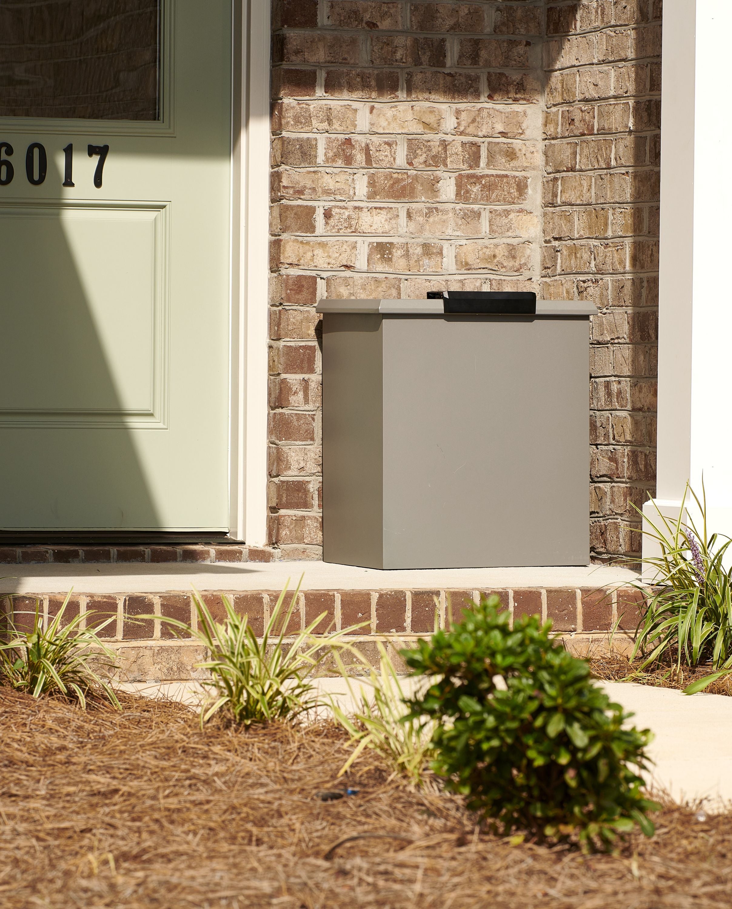 Loxx Boxx attached to a brick wall next to a house with a green door.